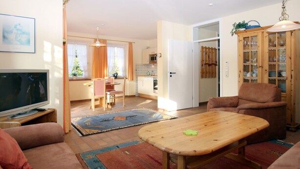Uma sala de estar com televisão, sofá, mesa de centro de madeira e um espaço de jantar com mesa e cadeiras.