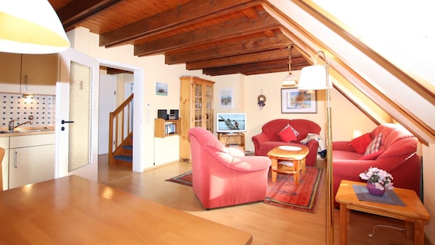 Ein gemütlicher Lofts-Wohnbereich mit Holzbalken, einer Küche, einem Esstisch und zwei roten Sofas.