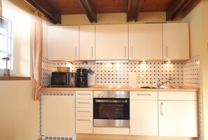 Uma cozinha compacta com armários brancos, forno embutido, micro-ondas e pia.