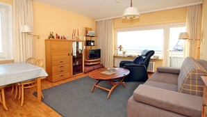 Un salon avec un canapé, une table à manger, un téléviseur et une vue sur la mer.