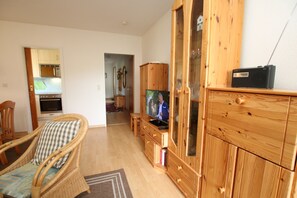 Un soggiorno con televisione, mobili in legno e una cucina sullo sfondo.