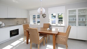 A modern kitchen with white cabinetry, a wooden dining table, wicker chairs, and a pendant light.