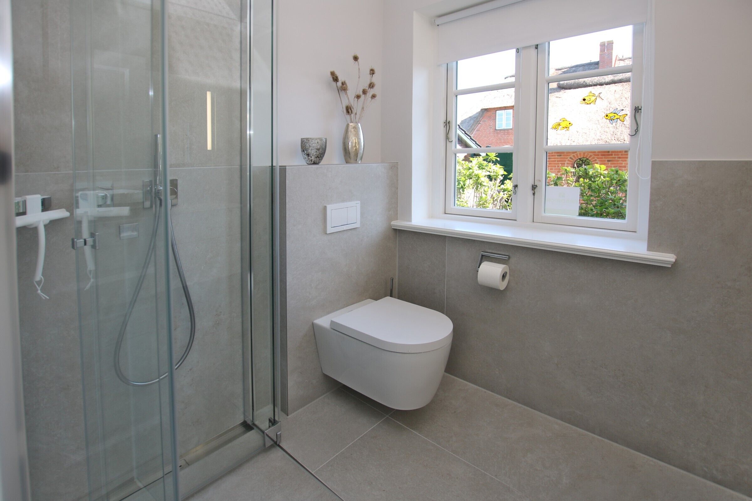 A modern bathroom with a glass shower enclosure, a white toilet, and a window with a view of the outside.