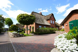A traditional brick house with a thatched roof, surrounded by a paved driveway and lush greenery. - Haushälfte in Wrixum Unter Reetdach mit 3- Zimmern und 90 qm (Wrixum)