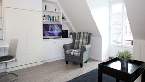 A modern living room with a television, a plaid armchair, a bookshelf, and a window. - Ferienwohnung mit 2- Zimmern auf ca. 35m² (Wyk auf Föhr)