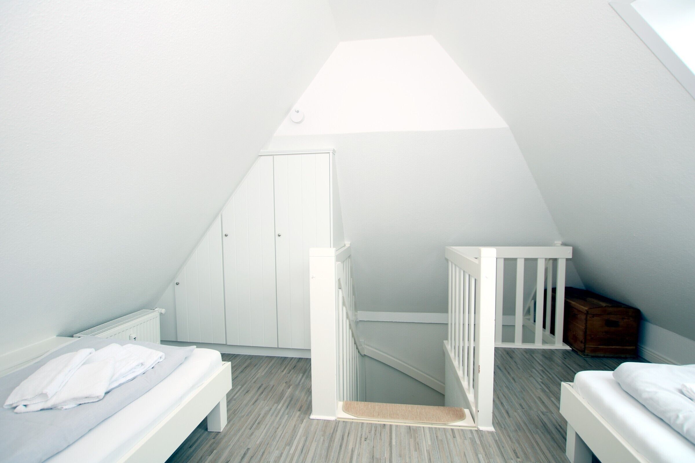 Una camera da letto piccola e bianca in mansarda, con soffitto spiovente, un comò in legno e una culla bianca.