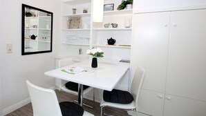 A modern, white room with a dining table, chairs, a mirror, and shelves with various items. - Ferienwohnung mit 2- Zimmern auf ca. 35m² (Wyk auf Föhr)