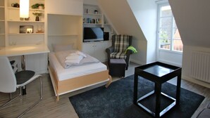 A modern bedroom with a bed, a desk, a chair, a TV, and a bookshelf. - Ferienwohnung mit 2- Zimmern auf ca. 35m² (Wyk auf Föhr)