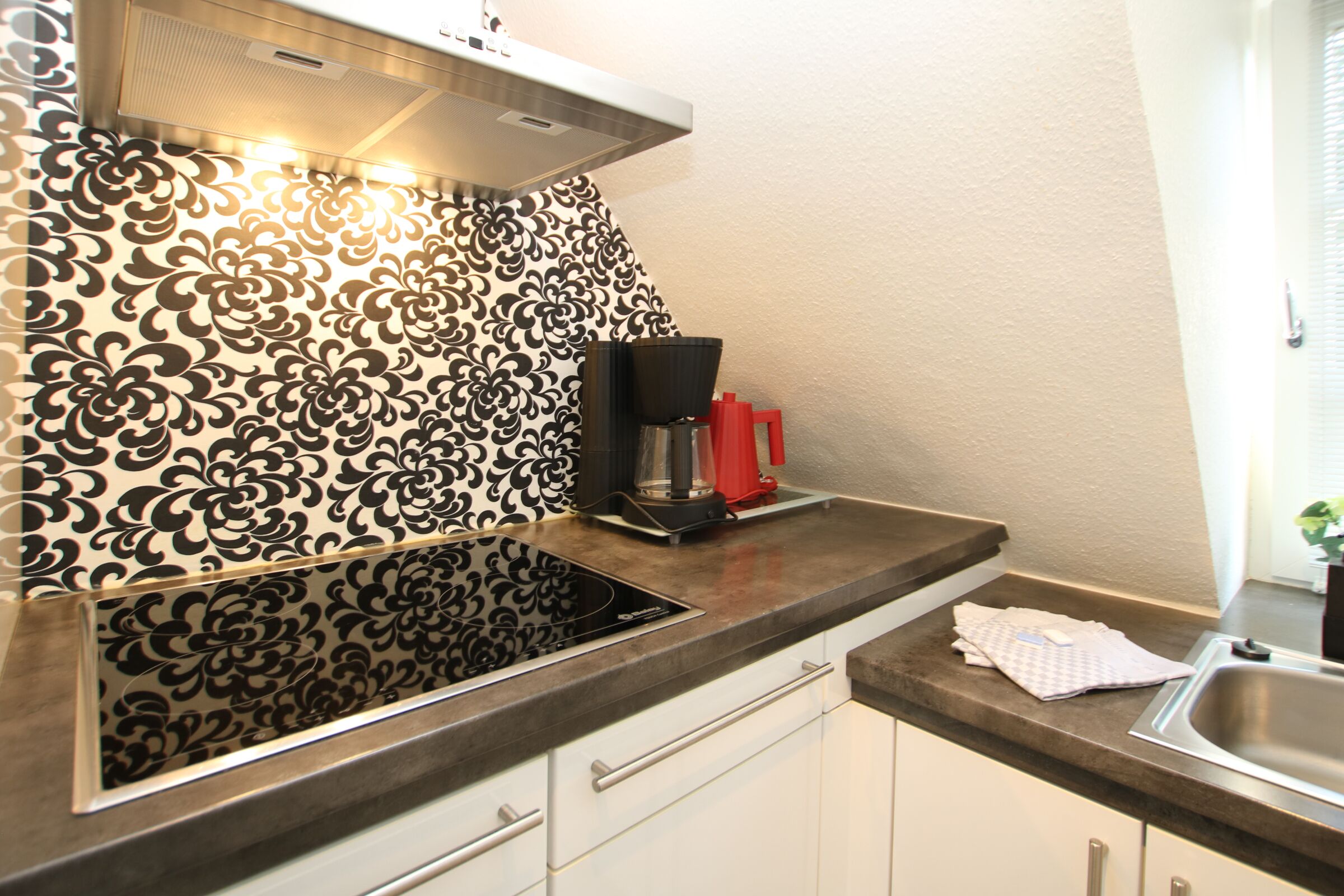 A kitchen with a patterned backsplash, a built-in stove, a coffee maker, and a sink.