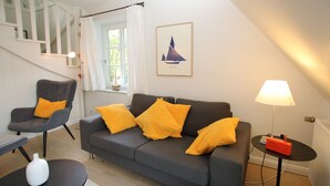 A living room with a grey sofa, two armchairs, a small black table, a white vase, a lamp, and a framed picture on the wall. - Ferienwohnung mit 2- Zimmern auf ca. 35m² (Wyk auf Föhr)