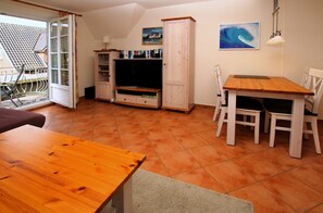 A room with a wooden table, white chairs, a cabinet, a television, and a painting on the wall.