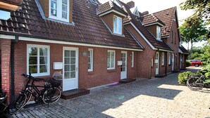 A brick house with a tiled roof, a bicycle parked outside, and a red car in the background. - Ferienwohnung mit 2- Zimmern auf ca. 35m² (Wyk auf Föhr)