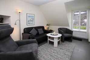 A modern living room with a sofa, armchair, and a small table with a candle. - Ferienwohnung mit 2- Zimmern auf ca. 35m² (Wyk auf Föhr)
