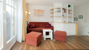 A living room with a sofa, ottomans, a small table, a bookshelf, and a staircase.