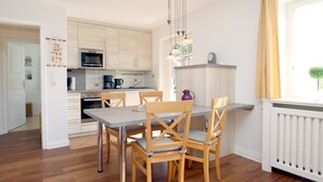 A modern kitchen with wooden cabinets, a dining table with chairs, and a window with curtains.