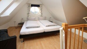 A bedroom with a bed, a window with curtains, a nightstand, and a wooden floor. - Ferienwohnung mit 3- Zimmern auf ca. 55m² für Max. 2 Erwachsene und 2 Kinder (Wyk auf Föhr)