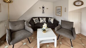 A living room with a sofa, two armchairs, a coffee table, and a decorative wall piece. - Ferienwohnung mit 3- Zimmern auf ca. 55m² für Max. 2 Erwachsene und 2 Kinder (Wyk auf Föhr)