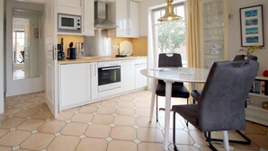 A modern kitchen with white cabinets, a microwave, oven, and a dining area with a round table and chairs. - Ferienwohnung mit 3- Zimmern auf ca. 55m² für Max. 2 Erwachsene und 2 Kinder (Wyk auf Föhr)