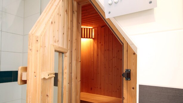 Una sauna de madera con un banco en el interior, una puerta y un panel de control en la parte superior.