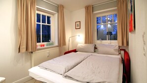Una cama doble con sábanas blancas, una mesita de noche, una lámpara y una ventana con cortinas.
