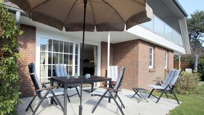 Un patio exterior con una mesa y sillas, un paraguas grande y una casa de ladrillo al fondo.