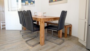 Un comedor con una mesa de madera y sillas negras, un taburete pequeño y un refrigerador al fondo.