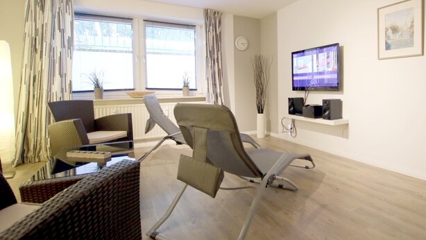 Una sala de estar moderna con un sillón reclinable, un sofá, un televisor y una ventana con cortinas.