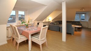 Un coin repas avec une table, des chaises et un vase de fleurs. On aperçoit un canapé et une lampe au fond.