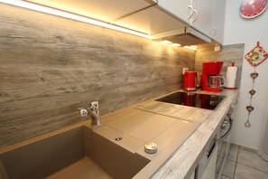 A kitchen with a wooden backsplash, stainless steel sink, and red appliances. - Ferienwohnung in Wyk, mit 2- Zimmern auf ca. 42qm im Erdgeschoß (Wyk auf Föhr)
