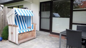 A patio area with a wicker chair with a striped canopy, a table, and a sliding glass door. - Ferienwohnung in Wyk, mit 2- Zimmern auf ca. 42qm im Erdgeschoß (Wyk auf Föhr)