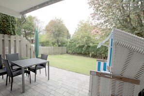Une terrasse avec une table et des chaises, une clôture en bois et une vue sur une pelouse.