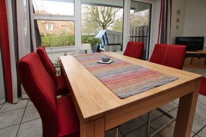 Un coin repas avec une table en bois, des chaises rouges, un tapis coloré et un téléviseur posé sur un meuble.