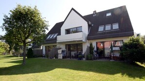 A two-story house with a covered patio area, a fenced yard, and a bicycle parked outside. - Ferienwohnung in Wyk, mit 2- Zimmern auf ca. 42qm im Erdgeschoß (Wyk auf Föhr)