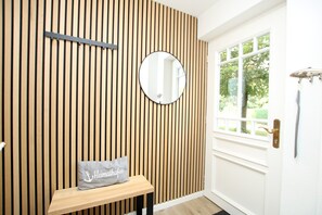 A room with a wooden slatted wall, a round mirror, a bench with a pillow, and a door with a window.