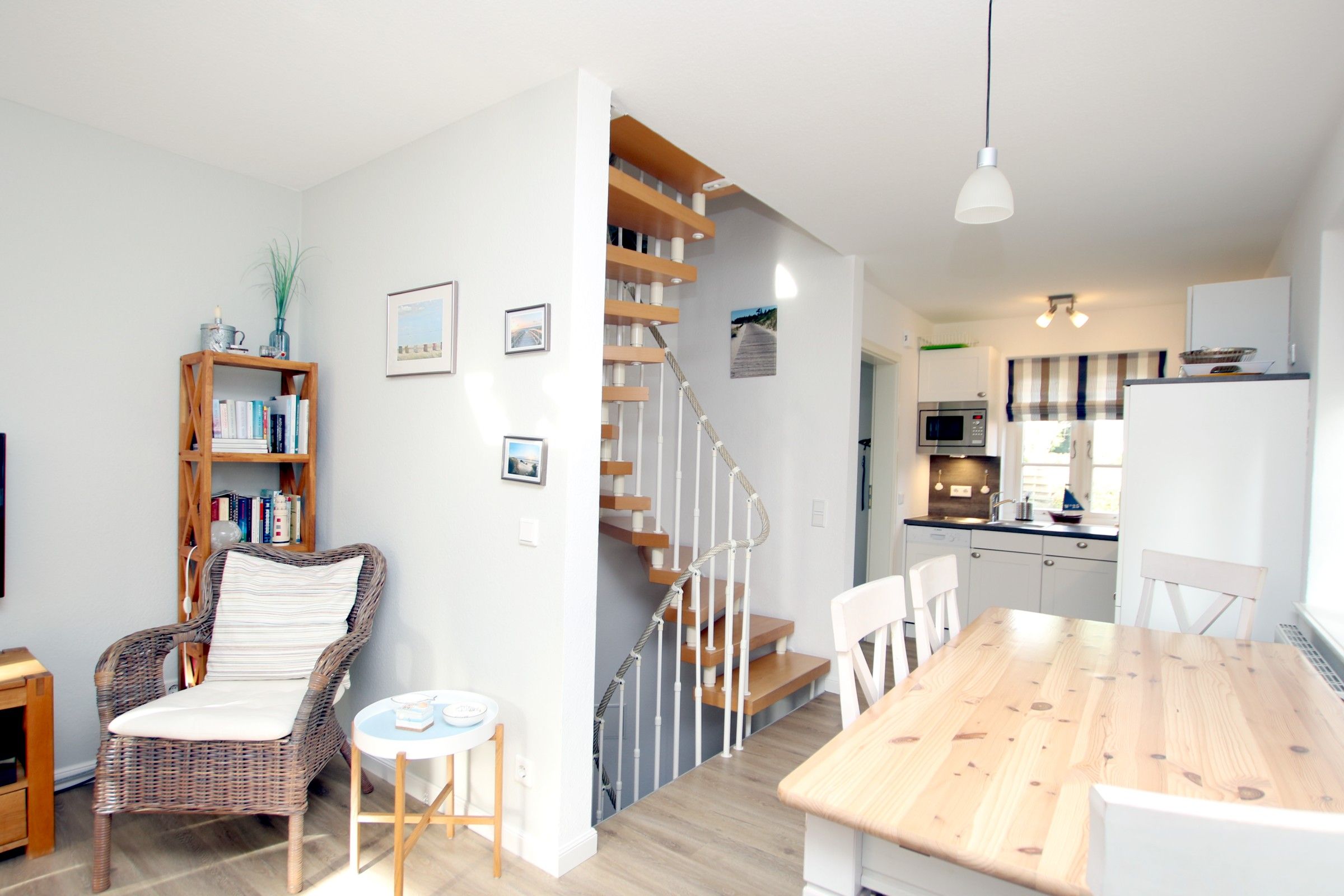 A modern kitchen with a dining area, a staircase, and a bookshelf.