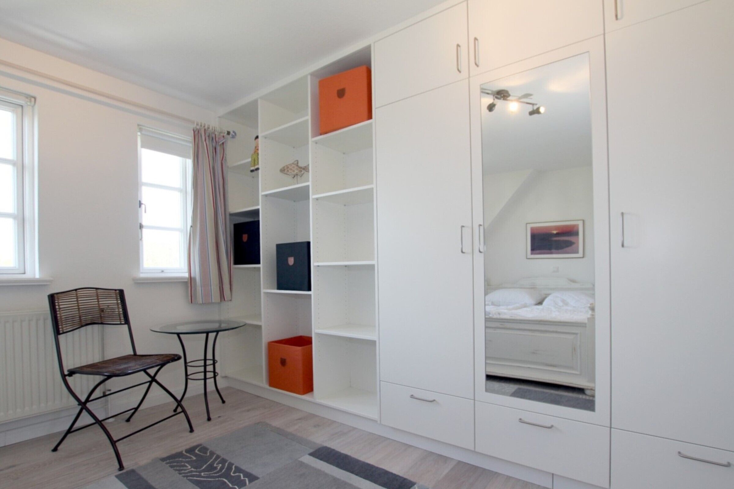 A bedroom with a bed, a wardrobe, a chair, a small table, and a radiator.
