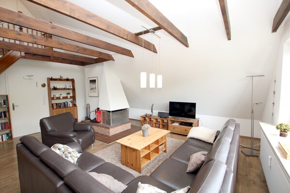 Ein modernes Wohnzimmer mit Kamin, Ledersofas, Fernseher und Holzbalken.
