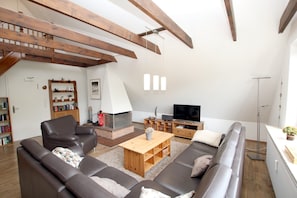 Uma sala de estar moderna com lareira, sofás de couro, televisão e vigas de madeira.