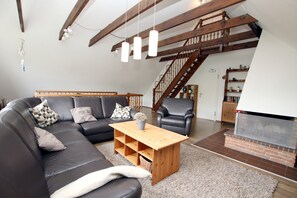Ein Wohnzimmer mit einer Eckcouch, einem Holztisch, einem Kamin und einer Treppe.