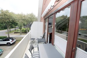 En balkon med et bord og stole, en parkeret bil og en bygning med store vinduer.