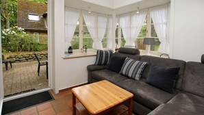 Ein Wohnzimmer mit einer Couch, einem Holztisch und Blick auf einen Garten durch große Fenster.