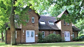Ein zweistöckiges Backsteinhaus mit einem steilen Satteldach, Dachgauben und einer Haustür mit einer kleinen Veranda.