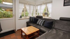 Ein Wohnzimmer mit einer Couch, einem Holztisch und einem Fenster mit Vorhängen.