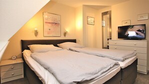 A bedroom with two beds, a TV, and a nightstand with a clock. - Haushälfte in Wrixum Unter Reetdach mit 3- Zimmern und 83 qm (Wrixum)