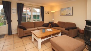 A living room with a sofa set, a coffee table, a fireplace, and a window with curtains. - Haushälfte in Wrixum Unter Reetdach mit 3- Zimmern und 83 qm (Wrixum)