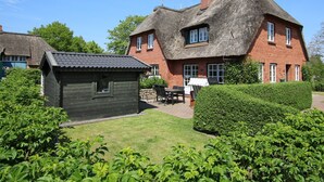 A traditional house with a thatched roof and a small wooden structure in the yard. - Haushälfte in Wrixum Unter Reetdach mit 3- Zimmern und 83 qm (Wrixum)