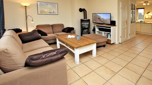 A living room with a sofa, a coffee table, a TV, and a fireplace. - Haushälfte in Wrixum Unter Reetdach mit 3- Zimmern und 83 qm (Wrixum)