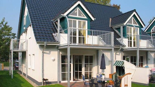 A two-story house with a balcony, a patio with outdoor furniture, and a well-maintained lawn. - Ferienwohnung mit 3- Zimmern Über ca. 100m² im Obergeschoß und Spitzboden (Wyk auf Föhr)