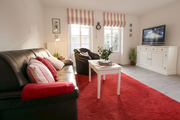 Ein Wohnzimmer mit einer Ledersofa, einem roten Teppich, einem weißen Tisch, einem Fernseher und einem Schrank.
