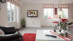 Ein Wohnzimmer mit Fernseher, weißen Schränken, einem roten Teppich und einer Pflanze.